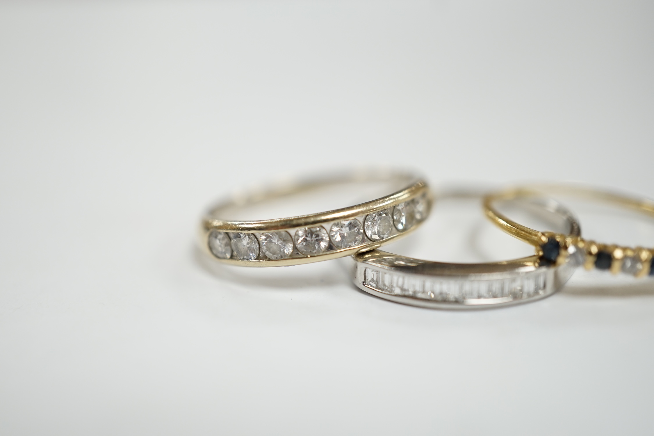 A white metal (stamped 950) and thirteen stone channel set baguette cut diamond ring, size O, together with two other unmarked gem set rings including diamond half eternity ring.